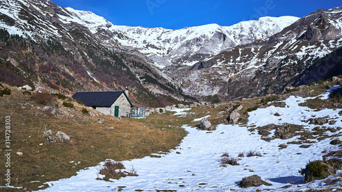 Winter landscape of a valley with snow, a shepherd's hut and mountains in the background