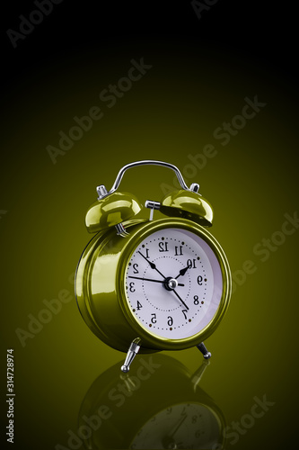 Yellow alarm clock with reflection on glass close-up isolated on dark background with yellow gradient.