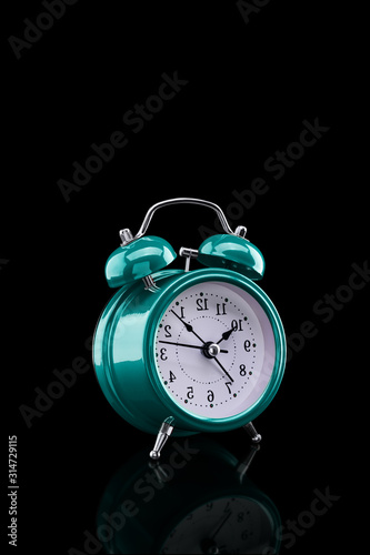 Turquoise alarm clock with reflection on glass close-up isolated on dark background.