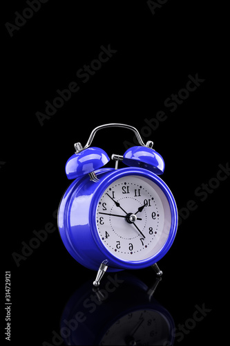 Blue alarm clock with reflection on glass close-up isolated on dark background.