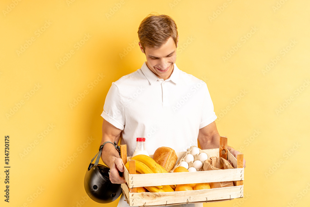 portrait of young courier carrying fresh food, vegetables and fruit, wearing white uniform with helmet for motorcycle, express delivery concept portrait of young courier carrying fresh food, vegetables and fruit, wearing white uniform with helmet for motorcycle, express delivery concept