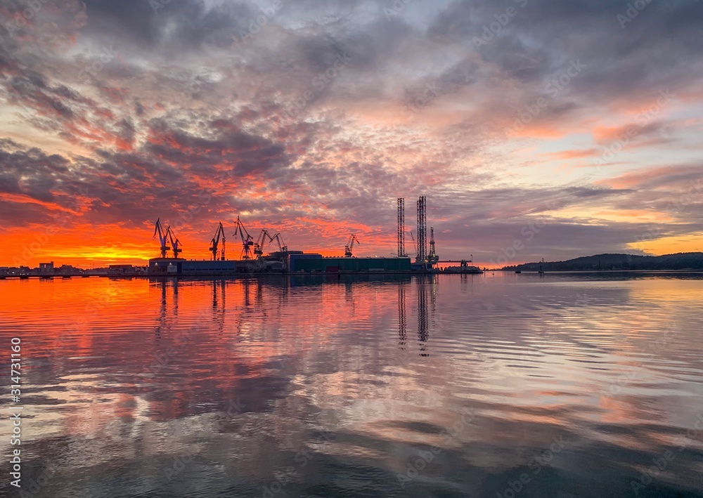 Silhouettes of cranes in the sea port, fantastic sunset, reflection on the water
