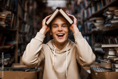 Happy student with book above his head, funny and joyful concept, smiley face of caucasian man student teenager. Love of education, reading books in library. Lifestyle people, enjoying time alone.