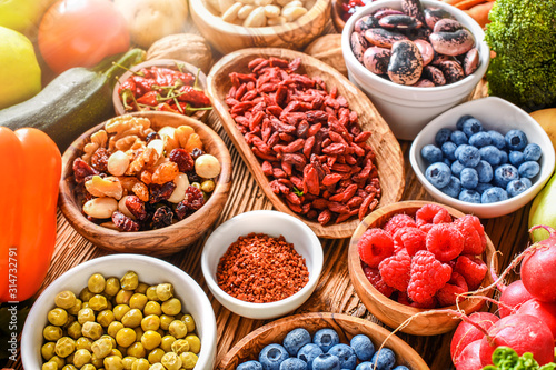 Healthy food eating variety selection in bowls: vegetables, fruits, berries, seeds, superfood, cereal, leaf vegetable on colorful background.