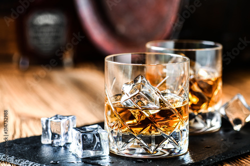 Canvas Print Glass of whiskey with ice cubes on black stone table