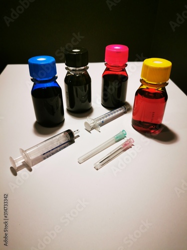 tubes of paint and brushes Refill inks for printers and copiers with blue, red, yellow and black ink in bottles with syringes to pull on and needles on a white background and black background