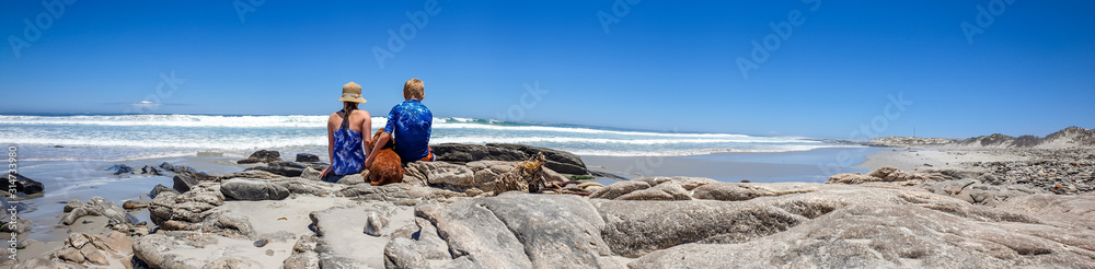Boy, girl and dog, sitting on a rocky beach, facing the ocean