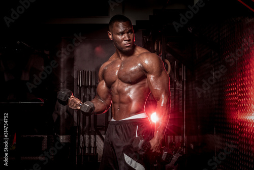 Obraz na płótnie Muscular African American, black shirtless , sweaty male bodybuilding athlete does barbell curls in a dark grungy gym with dramatic lighting flare w salonie