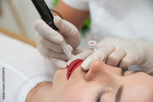Linergistka wykonuje makijaż permanentny ust, zbliżenie. Usta po makijażu permanentnym w salonie kosmetycznym. Mikropigmentacja ust zabieg w klinice medycyny estetycznej. 