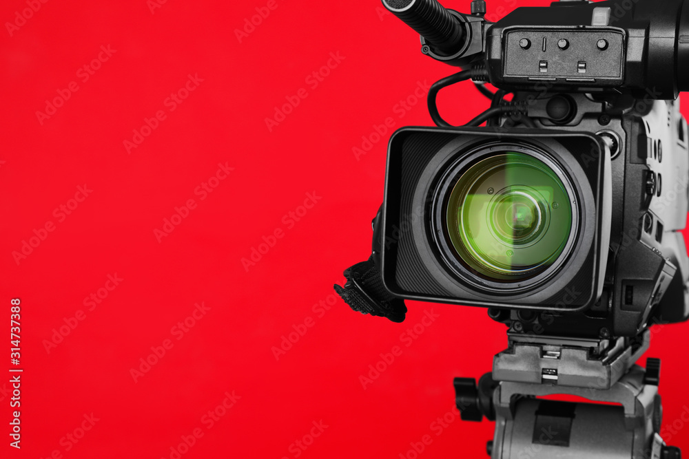 Modern professional video camera on red background, closeup. Space for text
