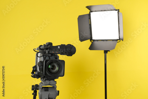 Professional video camera and lighting equipment on yellow background