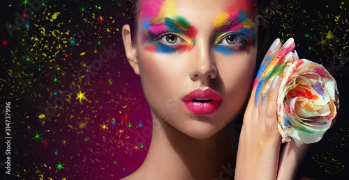 Obraz Beautiful girl with festive bright multi-colored make up  on the face. Young woman dressed in extravagant art makeup .Twinkling stars on a black background. Holiday ,celebration, cosmetic and beauty .