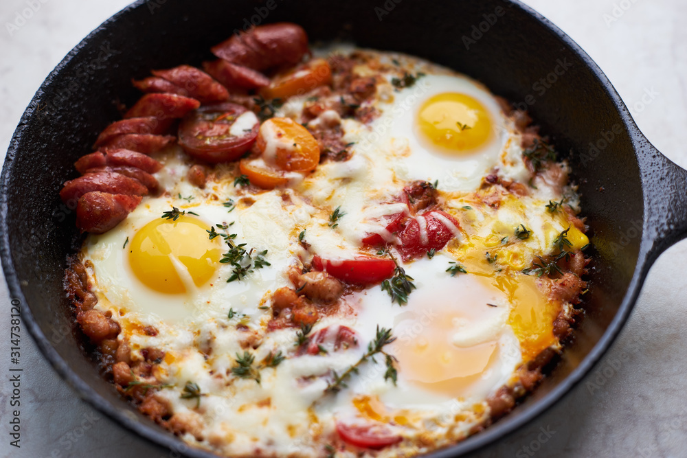 Hot homemade fried eggs with tomatoes and sausage in a pan closeup Hot homemade fried eggs with tomatoes and sausage in a pan closeup