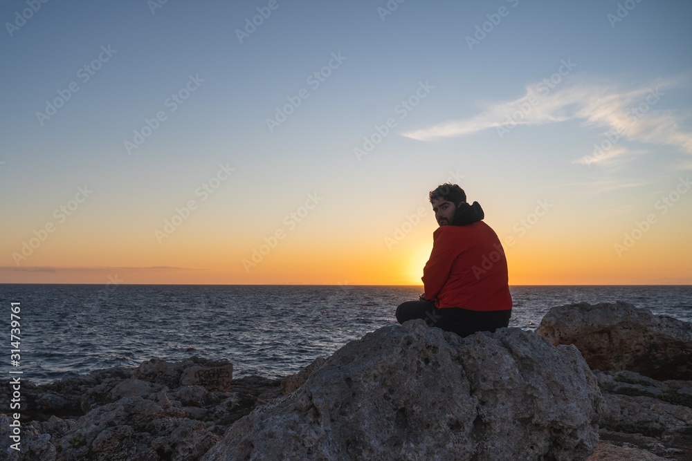 Man sitting on a rock at sunset and turning his face towards the camera