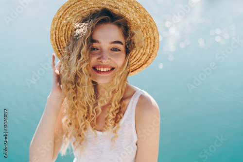 laughs joyfully, revealing a beautiful smooth teeth girl in a hat on a background of water