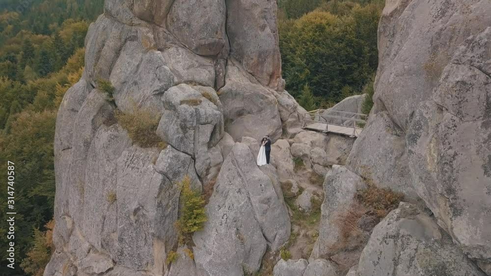 Newlyweds stand on a high slope of the mountain. Groom and bride. Aerial view Newlyweds stand on a high slope of the mountain. Groom and bride. Aerial view