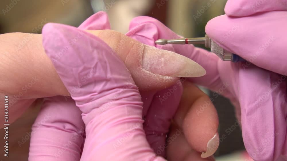 Close-up shot of hardware manicure in a beauty salon. Manicurist is applying electric nail file drill for trim cuticles on female fingers Close-up shot of hardware manicure in a beauty salon. Manicurist is applying electric nail file drill for trim cuticles on female fingers