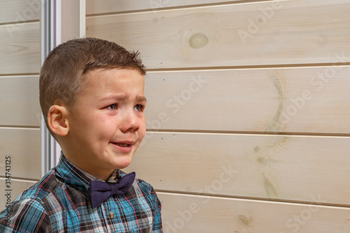 Bild auf Leinwand A 4 years old boy in a blue clerical shirt is crying on a light wooden background