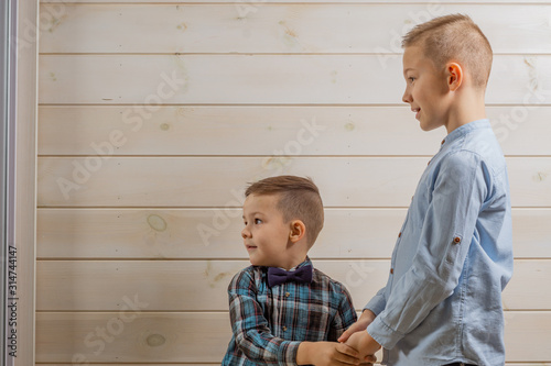 A 4-year-old boy in a blue klepy shirt cries on a light wooden background and his brother, 10 years old, is standing. photo