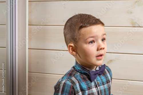 Foto A 4 years old boy in a blue clerical shirt is crying on a light wooden background