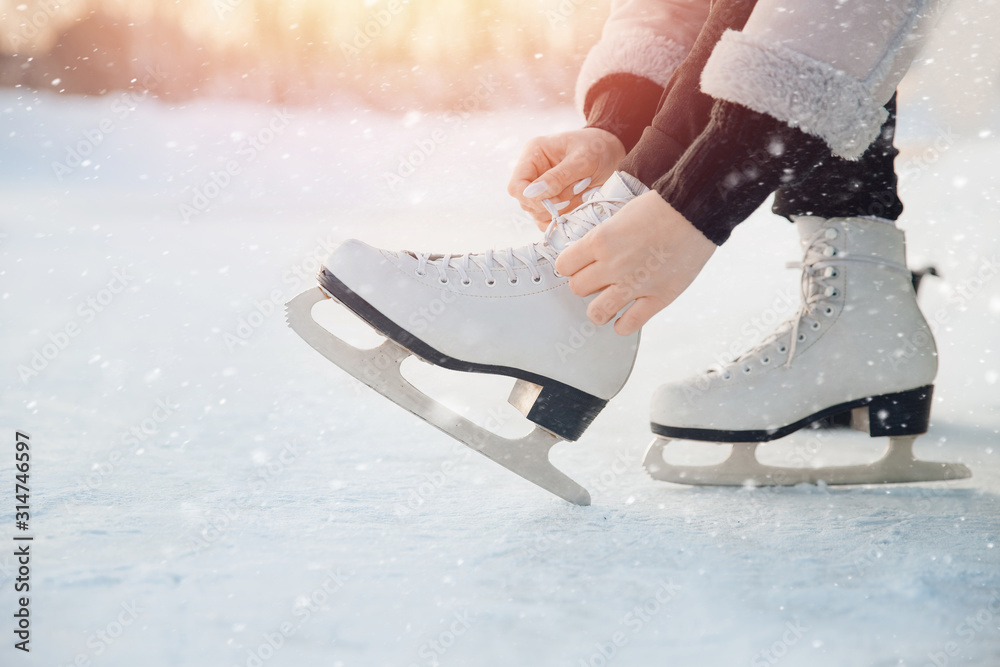 Girl ties shoelaces on white figure skates for ice rink in winter. Christmas holidays concept - obrazy, fototapety, plakaty 