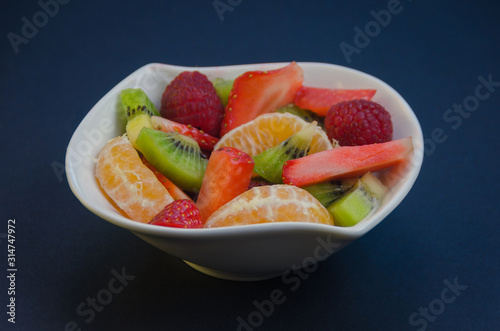 Fresh fruit dessert in a white bowl. Fruit salad made with kiwi, tangerine, raspberries and strawberries.