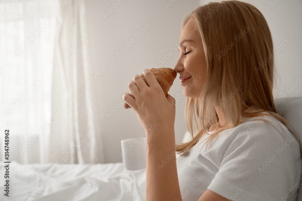 Girl smelling croissant in bed. Girl smelling croissant in bed.