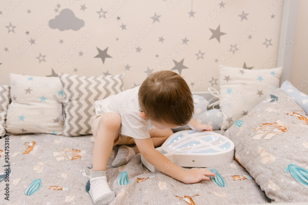 Little cute baby boy sitting in the children room in a wooden bed house with night lights in the shape of a balloon Little cute baby boy sitting in the children room in a wooden bed house with night lights in the shape of a balloon