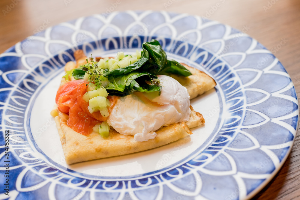 Savory crepes with salmon and poached egg.Tasty breakfast with pancakes, smoked salmon, pouched egg with spinach,Lettuce, onion, Hollandaise sauce.Fresh, healthy breakfast . Savory crepes with salmon and poached egg.Tasty breakfast with pancakes, smoked salmon, pouched egg with spinach,Lettuce, onion, Hollandaise sauce.Fresh, healthy breakfast .