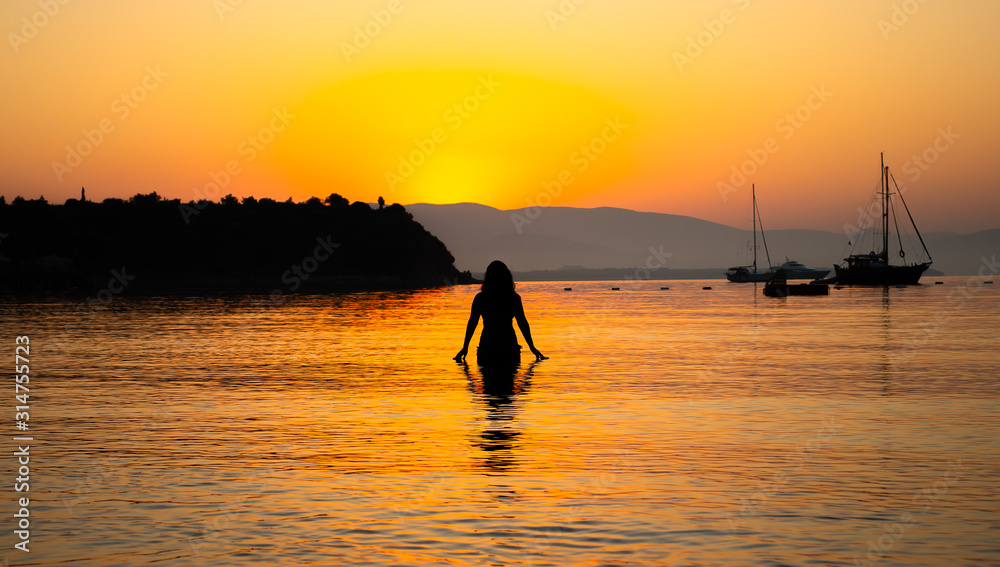 A young woman in the sea and the view of sunrise