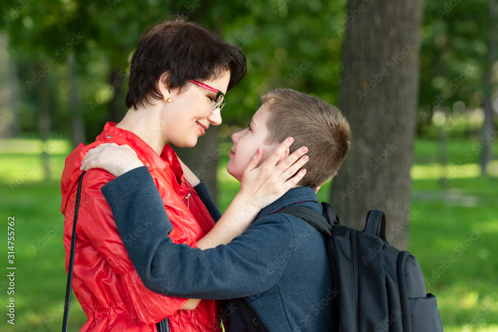 Mother and son hugging with love look at each other. Portrait of mom and son with a school backpack, go from school. Mother and son hugging with love look at each other. Portrait of mom and son with a school backpack, go from school.