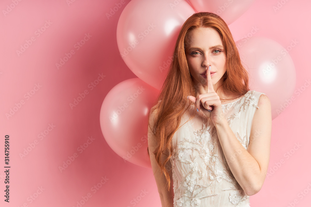 Beautiful flirty woman with auburn hair stand in coquettish gesture. Pink air balloons behind.Pink isolated background Beautiful flirty woman with auburn hair stand in coquettish gesture. Pink air balloons behind.Pink isolated background