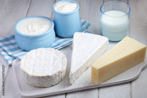Dairy - three types of cheese, milk, and yogurt on white wooden background