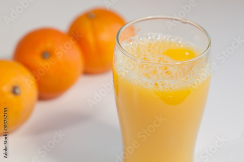Glass of orange juice on a table with oranges on the background.