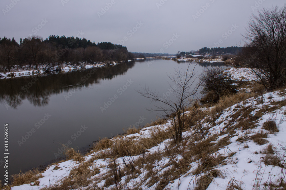 Winter landscape with river and reflections and snow on the Bank on a cloudy day