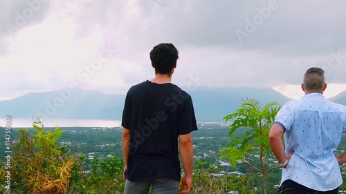 to men hot from a morning walk stop to look at the view of cairns with clouds covering the mountains in the distance, walk off left of frame photo