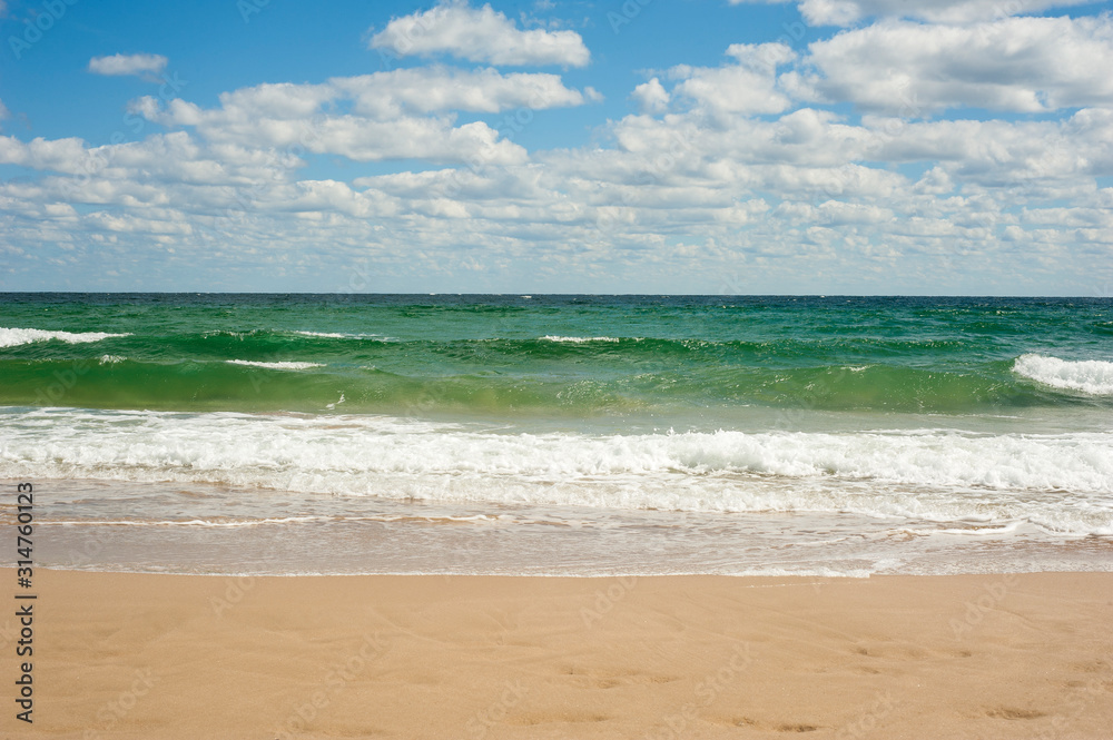 Blue sea wave on sandy beach. Beautiful sea waves on a background of blue sky with clouds on a sunny summer day. Sea waves roll on yellow sand.
