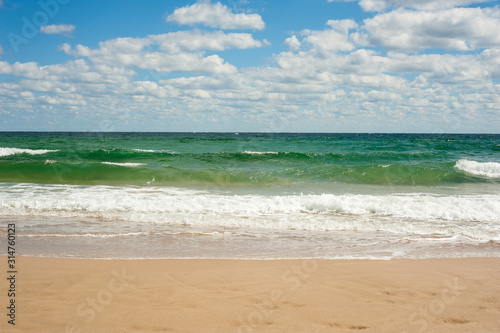 Blue sea wave on sandy beach. Beautiful sea waves on a background of blue sky with clouds on a sunny summer day. Sea waves roll on yellow sand.