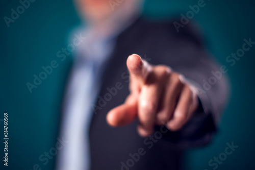 Businessman in suit point finger at camera in front of black background photo