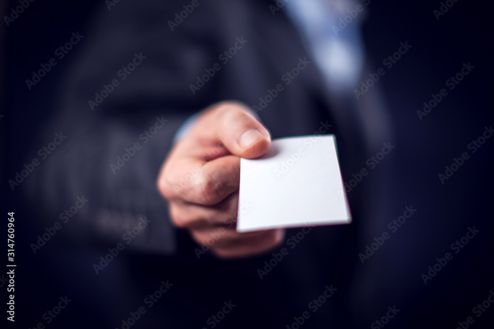 Businessman in suit holding business card in front of black background Businessman in suit holding business card in front of black background