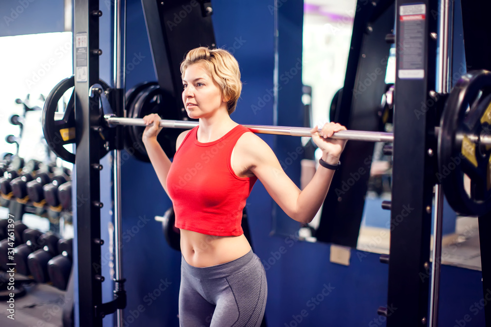 Woman in red top preparing to do squats in gym. People, fitness and lifstyle concept Woman in red top preparing to do squats in gym. People, fitness and lifstyle concept