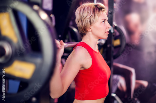 Woman in red top preparing to do squats in gym. People, fitness and lifstyle concept