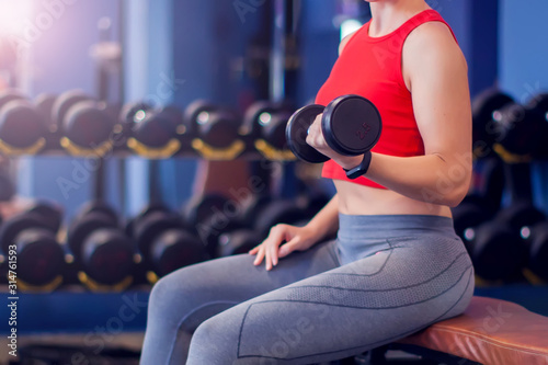 Woman in red top training bicep in gym. People, fitness and lifstyle concept