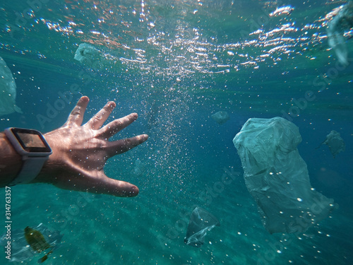 A man swimming among toxic plastic wastes floating in the ocean