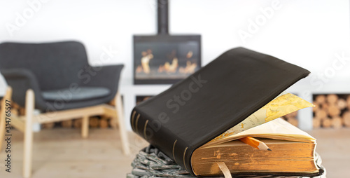 Bible book with pencil, on the background of the living room with a fireplace. Reading a book in a cozy environment.