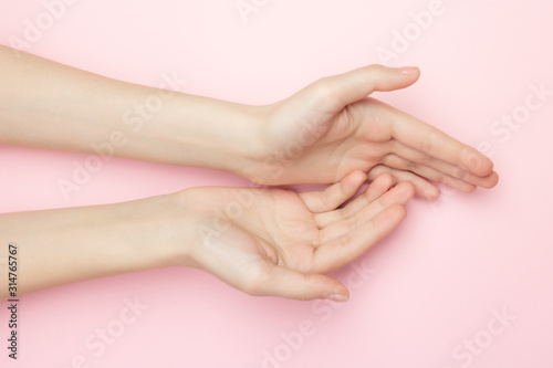 The woman hands on a pink background. Cosmetics for a sensitive skin care. Natural petal cosmetics  anti-wrinkle hand care. A thin wrist and natural manicure.