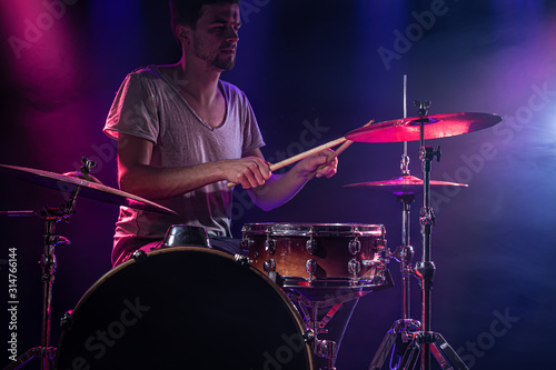 The drummer plays the drums. Beautiful blue and red background, with rays of light. Beautiful special effects smoke and lighting. The process of playing a musical instrument. Close-up photo.