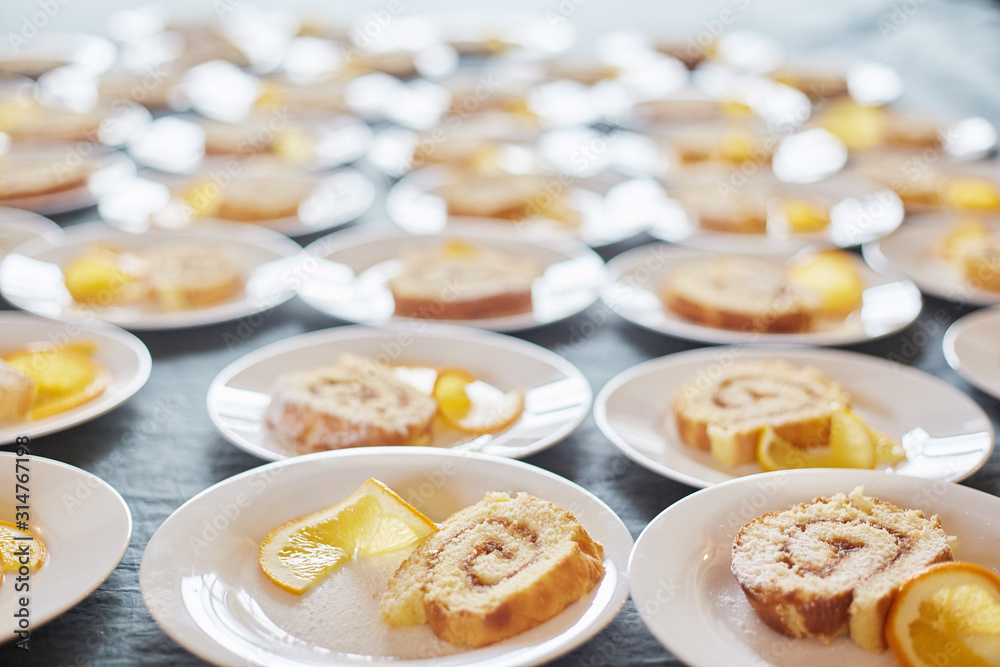 sponge rolls with jam and a slice of orange on white plates. background