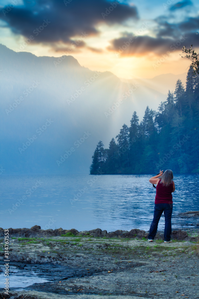woman with camera shooting pictuers along the edge of mountain lake at sunset