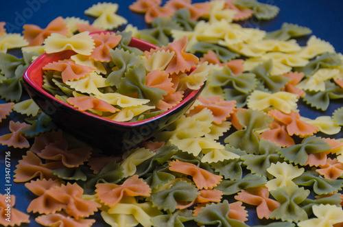 Bowl full of tri colors farfalle pasta. Pile of multicolored bow tie pasta on a blue background